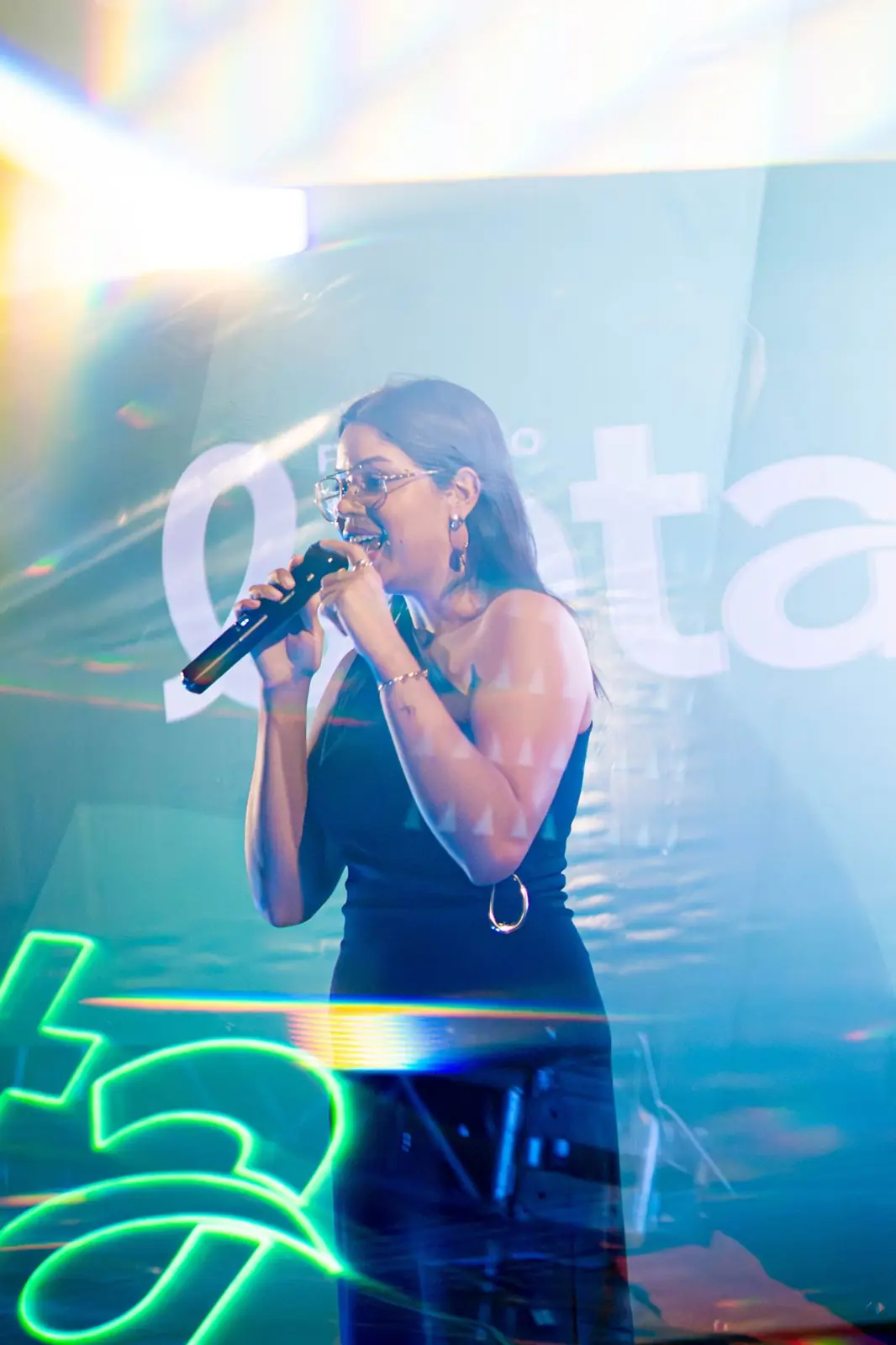 Bruna falando ao microfone em palco iluminado