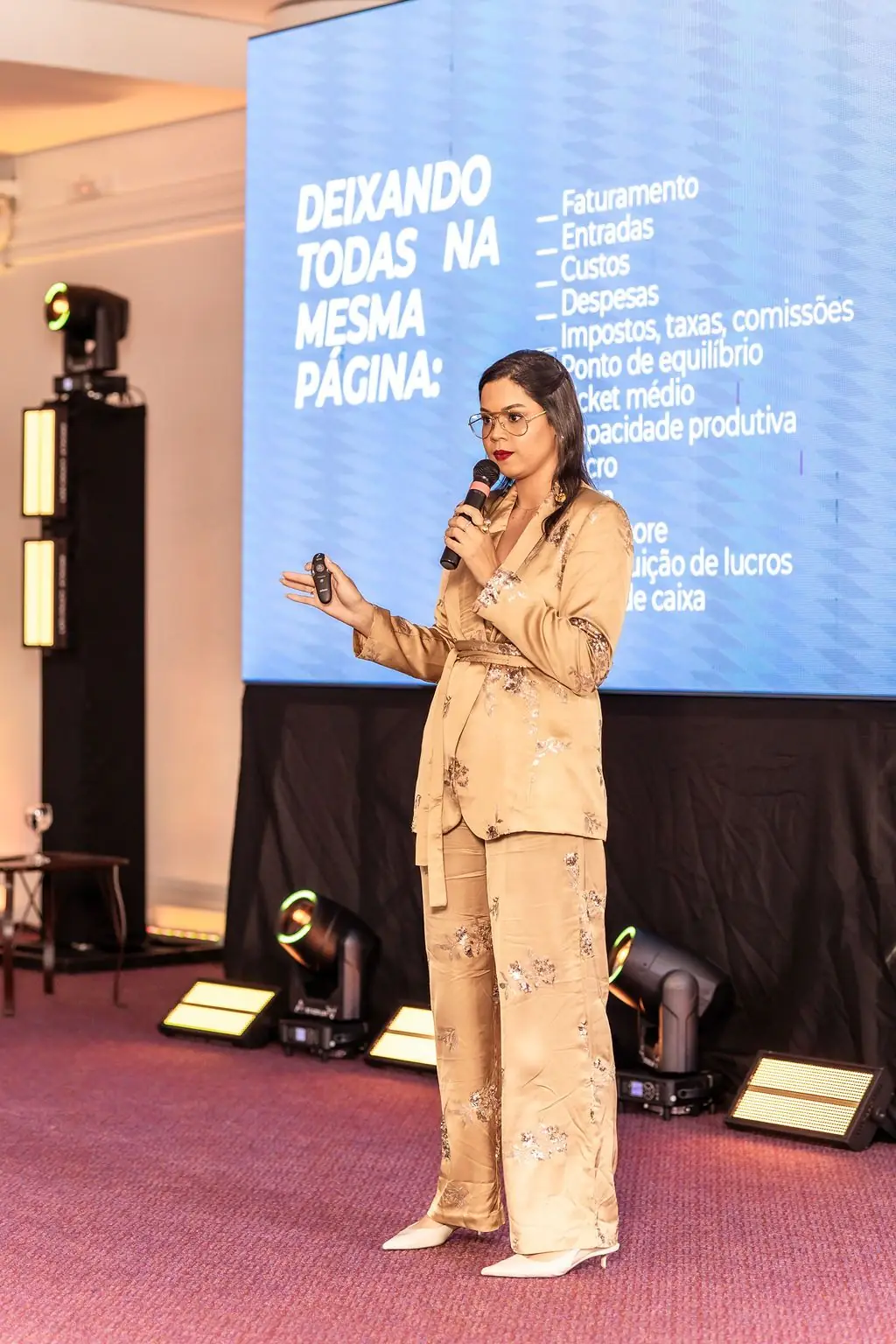 Bruna dos Santos no palco, apresentando um slide sobre faturamento, custos e ponto de equilíbrio