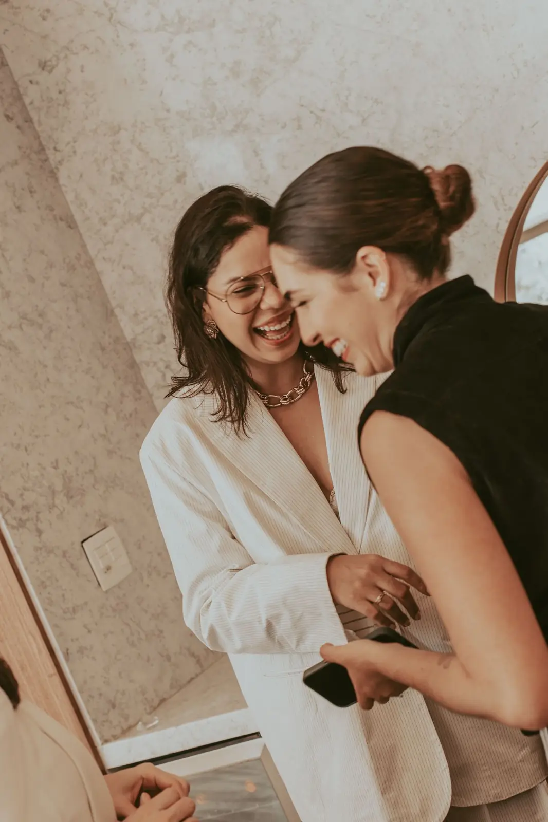 Bruna dos Santos de terno branco, rindo abraçada a uma cliente